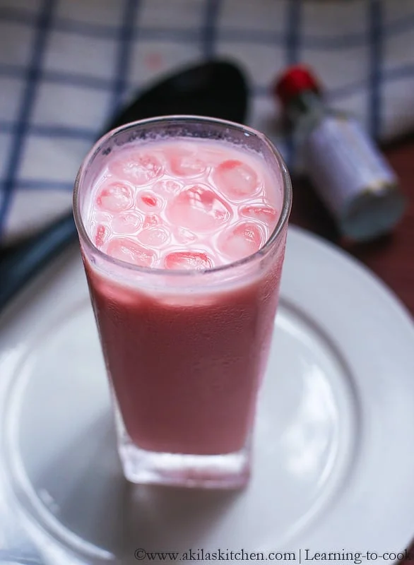 Rose Milk - Rose Milk Syrup A Tall Glass Of Pink, Cold Drink With Ice, Placed On A White Plate, In Dm Traders Organic Store.