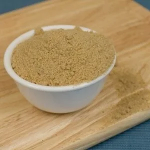 A White Bowl Filled With Brown Sugar On A Wooden Surface, Dm Traders Organic Store.