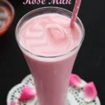 A tall glass of pink Rose Milk Syrup with a straw, rose petals, and the text "Rose Milk" on top, with the brand name "DM Traders Organic store".