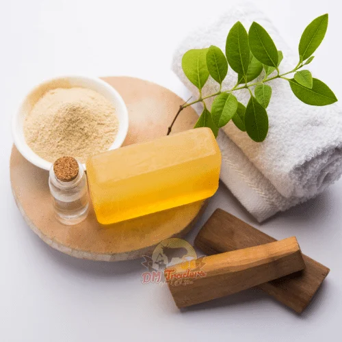 Sandalwood Soap A Display Of Sandalwood Soap Skincare Products Including A Soap Bar, A Bowl Of Powder, A Small Bottle, Fresh Green Leaves, Wooden Pieces, And A White Towel, Branded By Dm Traders Organic Store.
