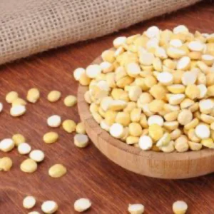 A wooden bowl filled with fried gram split, with some scattered on the wooden surface.